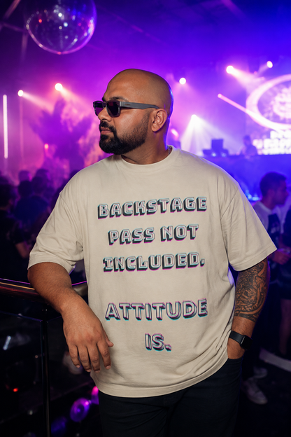 A man wearing a beige graphic t-shirt with the text 'BACKSTAGE PASS NOT INCLUDED. ATTITUDE IS.